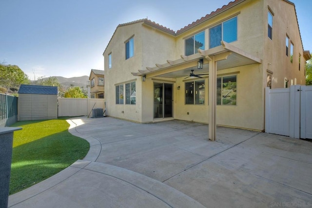 back of house featuring a mountain view, a lawn, a storage unit, a patio area, and central AC