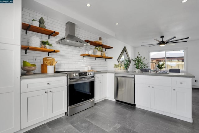 kitchen featuring wall chimney range hood, sink, white cabinetry, stainless steel appliances, and decorative backsplash