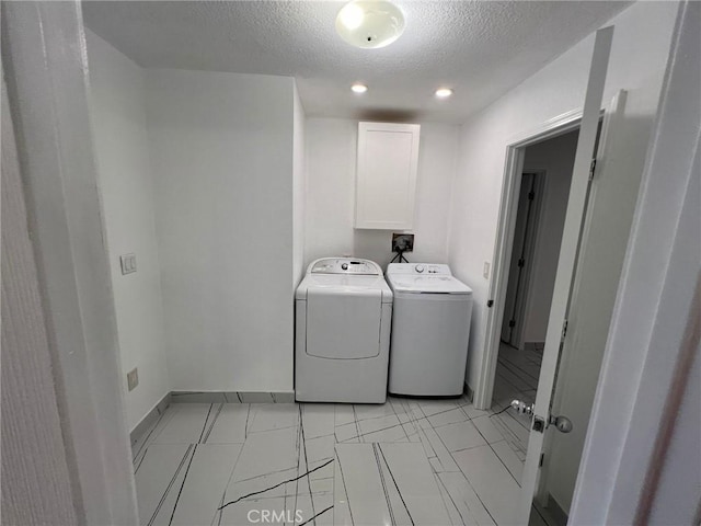 washroom with a textured ceiling, cabinets, and washing machine and clothes dryer