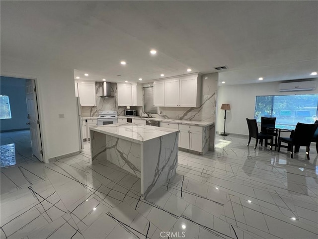 kitchen featuring wall chimney range hood, a kitchen island, a wall mounted air conditioner, appliances with stainless steel finishes, and white cabinets