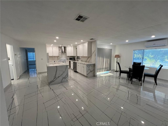 kitchen featuring an AC wall unit, a center island, white cabinetry, light stone countertops, and wall chimney exhaust hood