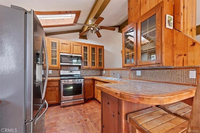 kitchen featuring decorative backsplash, vaulted ceiling with skylight, stainless steel appliances, ceiling fan, and sink