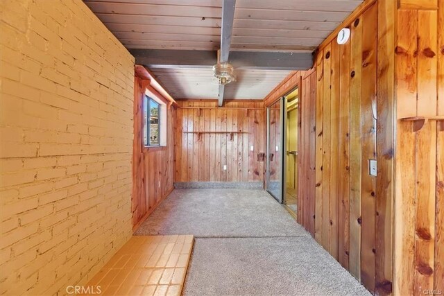 hallway featuring beam ceiling, wood walls, carpet flooring, and brick wall