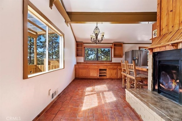 interior space with a wealth of natural light, hanging light fixtures, stainless steel fridge with ice dispenser, beamed ceiling, and a chandelier