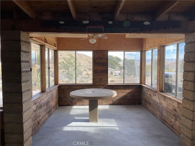 unfurnished sunroom with ceiling fan, a wealth of natural light, and beamed ceiling