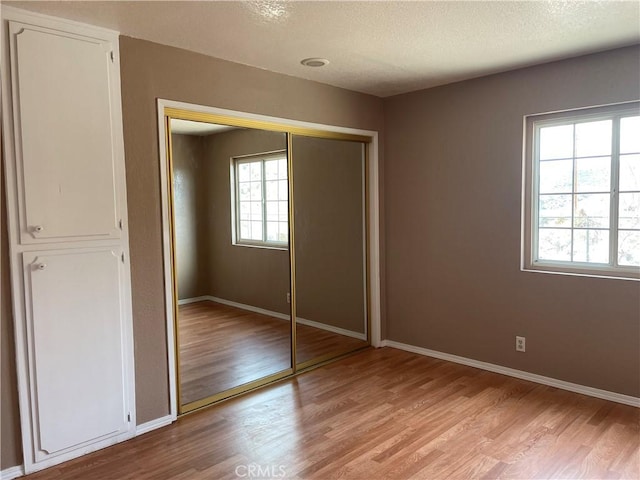 unfurnished bedroom featuring light wood-type flooring, a closet, a textured ceiling, and multiple windows