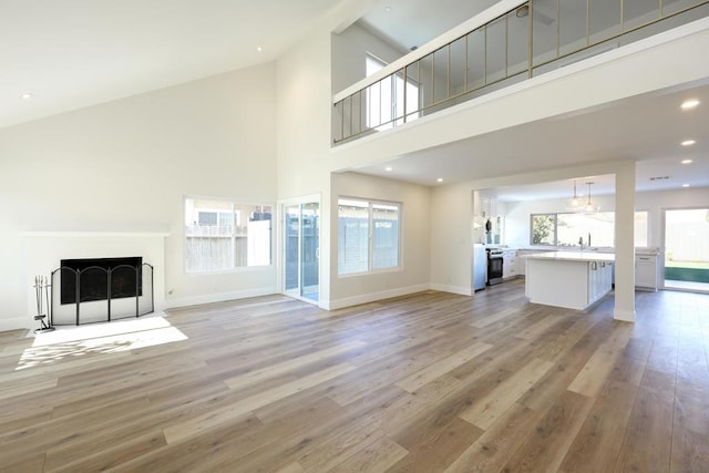 unfurnished living room featuring a high ceiling, sink, light hardwood / wood-style flooring, and plenty of natural light