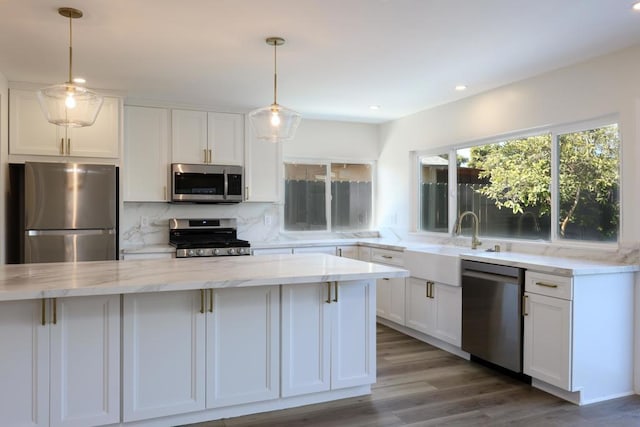 kitchen with light stone countertops, decorative light fixtures, white cabinetry, stainless steel appliances, and tasteful backsplash