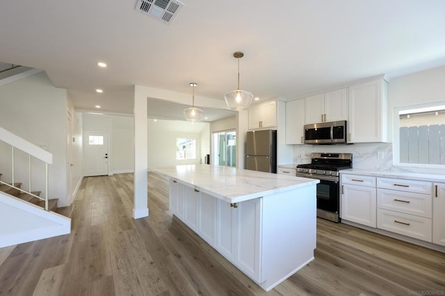 kitchen with pendant lighting, appliances with stainless steel finishes, a center island, white cabinetry, and decorative backsplash