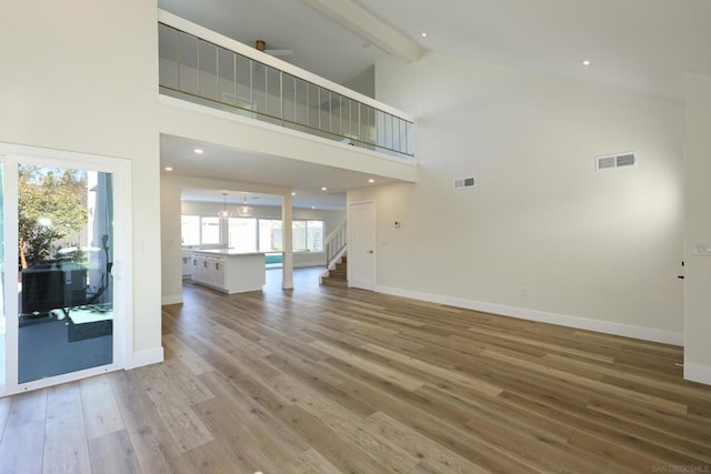 unfurnished living room featuring high vaulted ceiling, beam ceiling, ceiling fan, and wood-type flooring