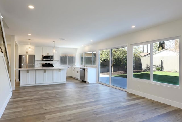 kitchen featuring a center island, white cabinetry, light hardwood / wood-style flooring, hanging light fixtures, and stainless steel appliances