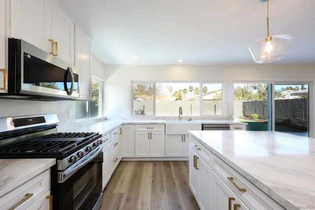 kitchen featuring white cabinetry, light stone counters, hanging light fixtures, and stainless steel appliances