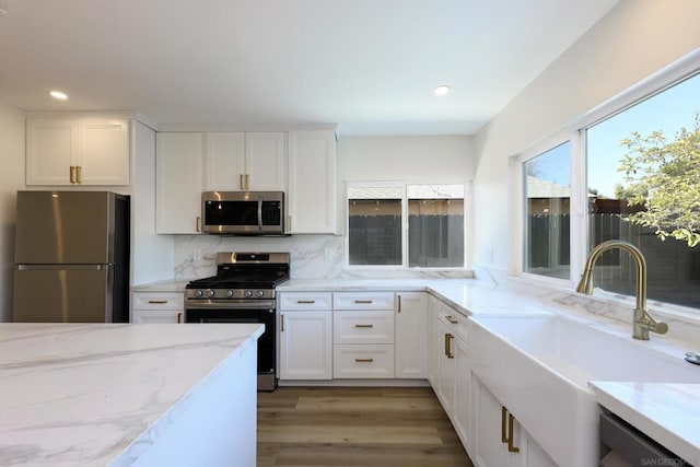 kitchen featuring white cabinetry, stainless steel appliances, decorative backsplash, light stone countertops, and sink