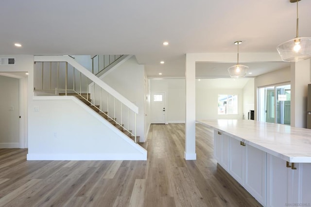 interior space with white cabinetry, light stone countertops, hanging light fixtures, and light wood-type flooring