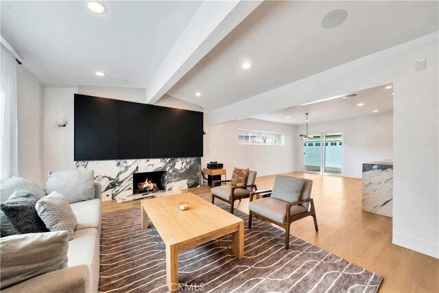 living room with a high end fireplace, light hardwood / wood-style floors, and vaulted ceiling with beams