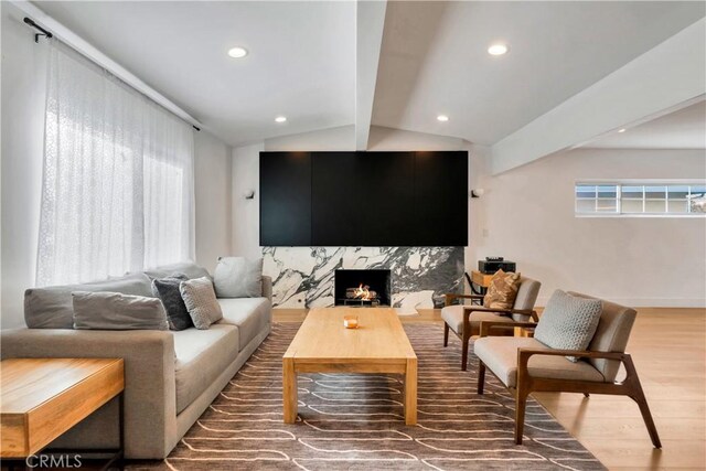 living room with a premium fireplace, vaulted ceiling with beams, a healthy amount of sunlight, and wood-type flooring