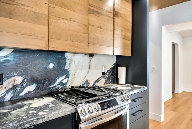 kitchen featuring light wood-type flooring, stainless steel gas range, tasteful backsplash, and dark stone counters