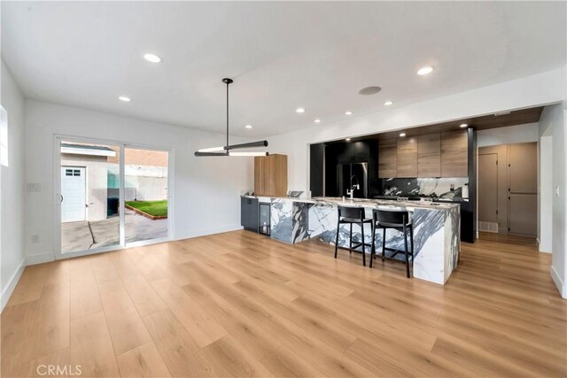 kitchen with decorative light fixtures, tasteful backsplash, light hardwood / wood-style floors, kitchen peninsula, and a breakfast bar area