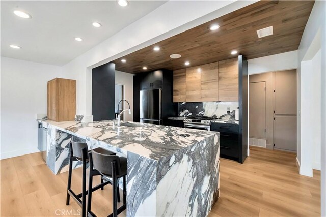 kitchen featuring light stone countertops, stainless steel appliances, decorative backsplash, a kitchen breakfast bar, and kitchen peninsula