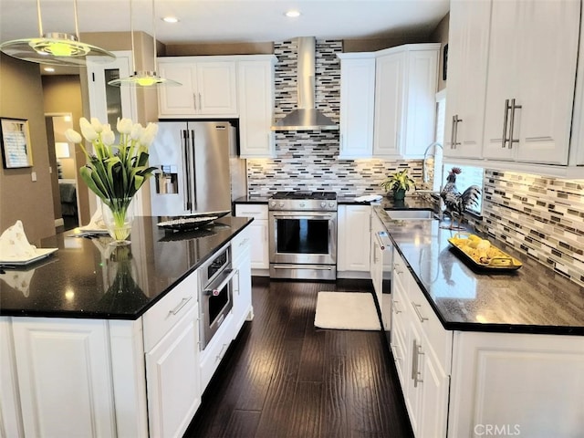 kitchen with stainless steel appliances, wall chimney exhaust hood, pendant lighting, white cabinets, and sink