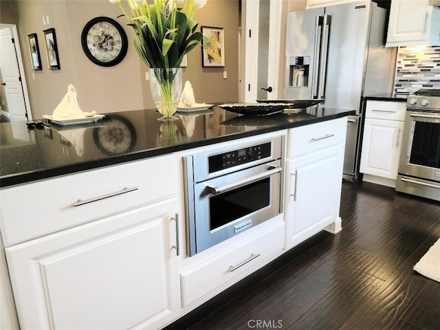 kitchen featuring dark stone countertops, decorative backsplash, white cabinetry, dark wood-type flooring, and appliances with stainless steel finishes