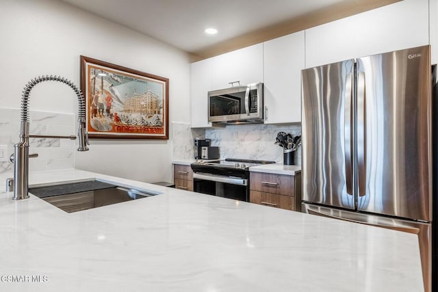 kitchen with appliances with stainless steel finishes, backsplash, light stone counters, sink, and white cabinets