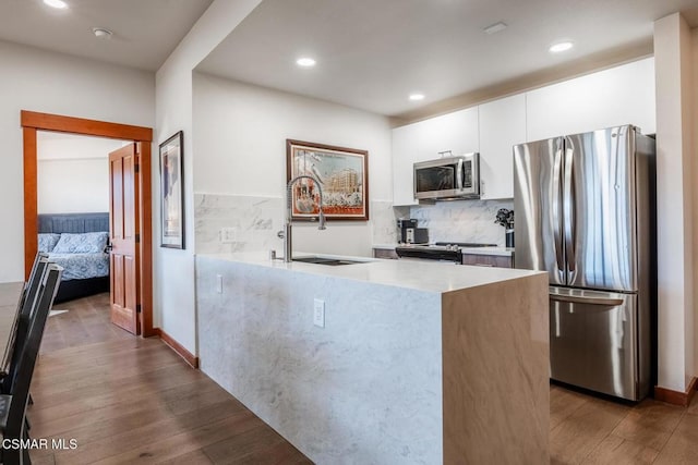 kitchen with hardwood / wood-style floors, sink, tasteful backsplash, white cabinetry, and stainless steel appliances