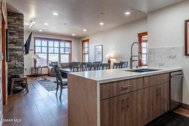 kitchen with dark wood-type flooring, sink, stainless steel dishwasher, decorative backsplash, and kitchen peninsula