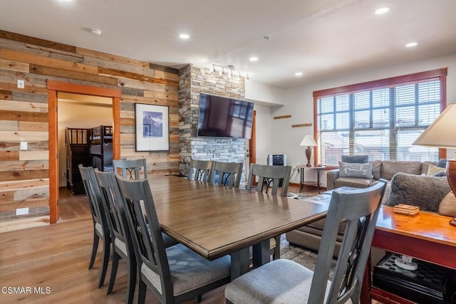 dining room with a stone fireplace, wooden walls, and light hardwood / wood-style flooring