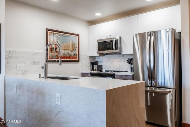 kitchen featuring backsplash, sink, white cabinetry, kitchen peninsula, and stainless steel appliances