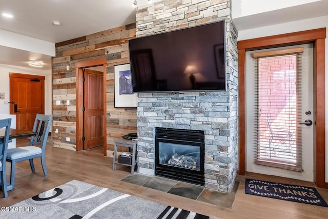 living room with wood walls, a stone fireplace, and wood-type flooring