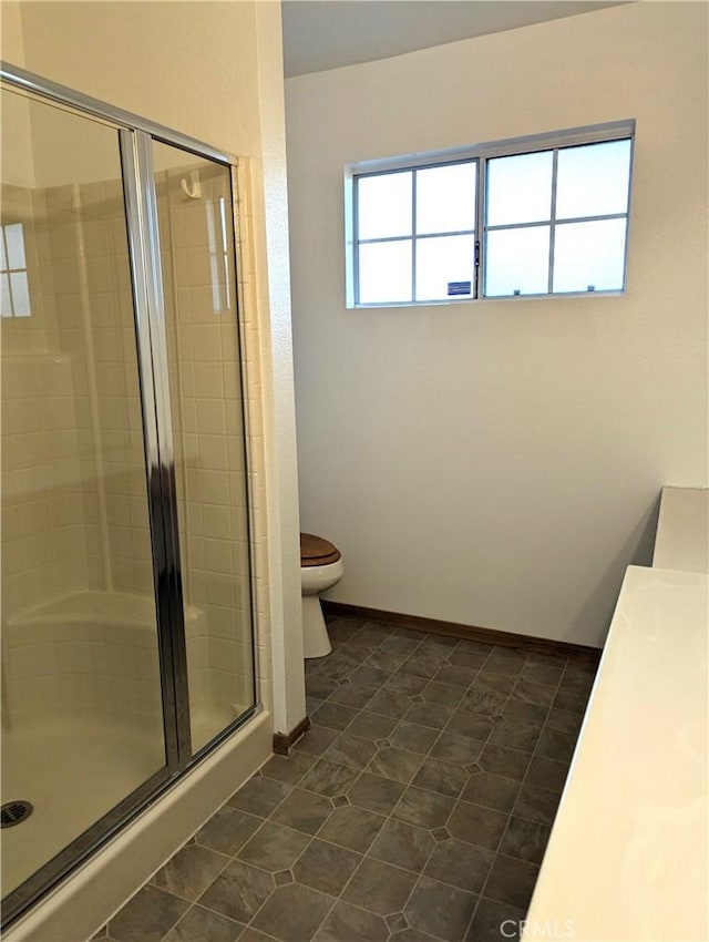 bathroom featuring baseboards, toilet, a shower stall, and tile patterned flooring