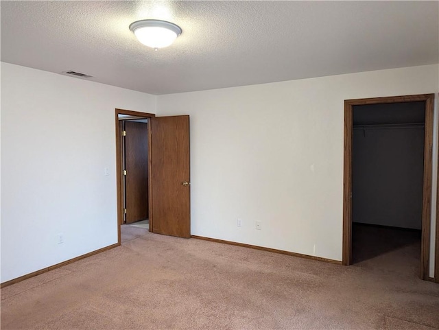 unfurnished bedroom featuring light carpet, a closet, a spacious closet, and a textured ceiling