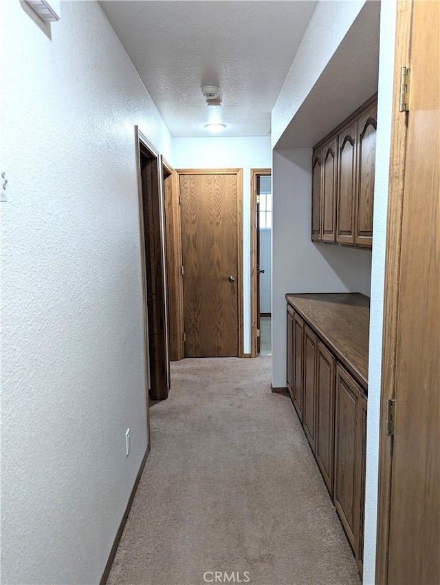 corridor with light colored carpet and a textured ceiling