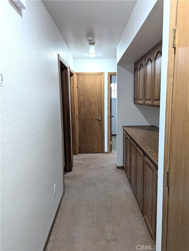 corridor with light colored carpet, baseboards, a textured wall, and a textured ceiling