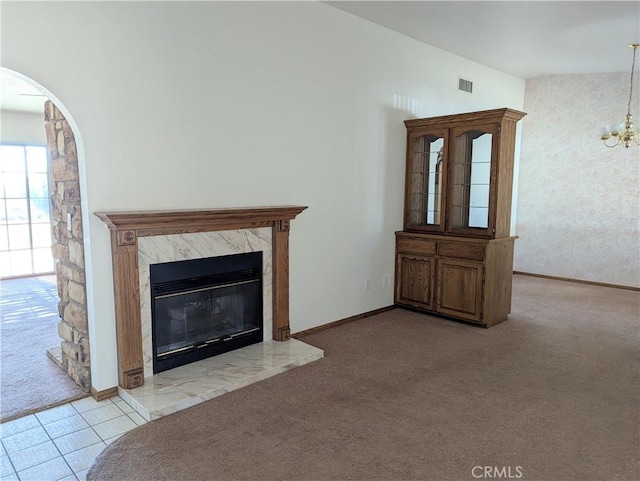 unfurnished living room featuring a high end fireplace, visible vents, baseboards, carpet floors, and arched walkways