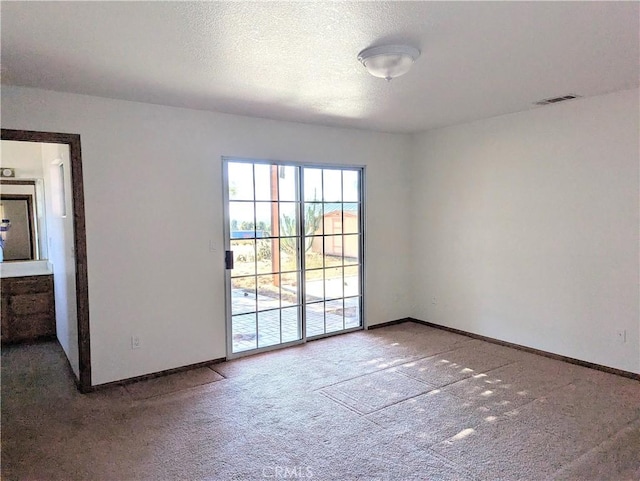 carpeted spare room featuring visible vents, baseboards, and a textured ceiling