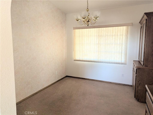 unfurnished room with a notable chandelier, baseboards, and carpet