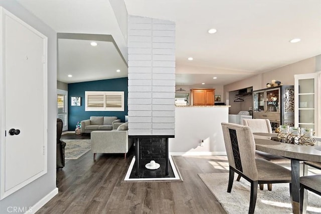 dining space featuring a multi sided fireplace, dark wood-type flooring, lofted ceiling, and ornate columns