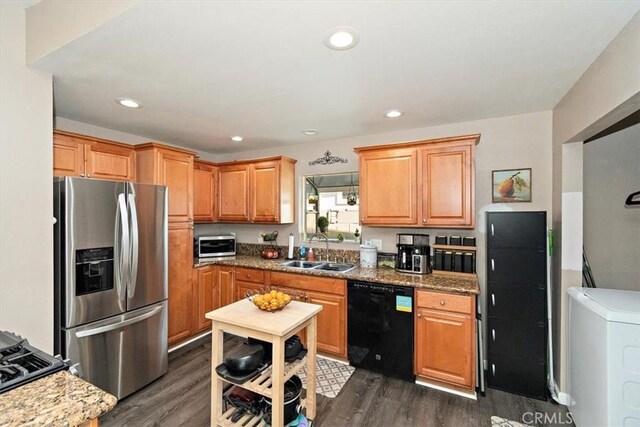 kitchen with appliances with stainless steel finishes, washer / dryer, dark hardwood / wood-style flooring, sink, and light stone counters