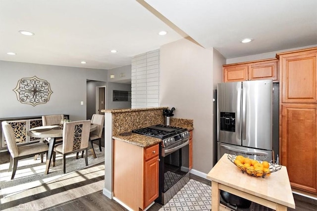 kitchen with dark wood-type flooring, appliances with stainless steel finishes, kitchen peninsula, and light stone counters