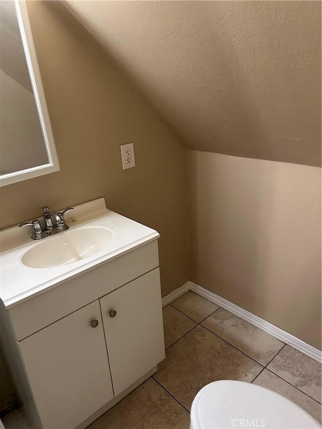 bathroom with tile patterned floors, toilet, vanity, and lofted ceiling