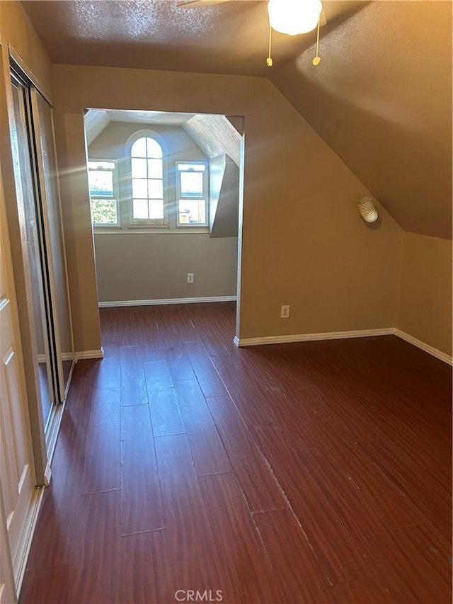 additional living space with a textured ceiling, vaulted ceiling, and dark hardwood / wood-style floors