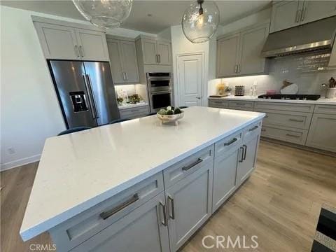 kitchen featuring a kitchen island, stainless steel appliances, tasteful backsplash, hanging light fixtures, and light hardwood / wood-style flooring