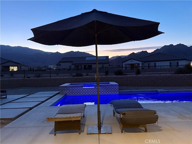 pool at dusk with an in ground hot tub, a mountain view, and a patio