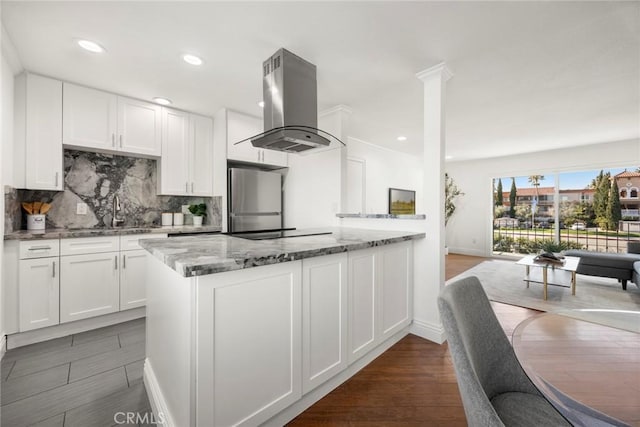 kitchen with stainless steel refrigerator, white cabinetry, sink, island exhaust hood, and light stone countertops