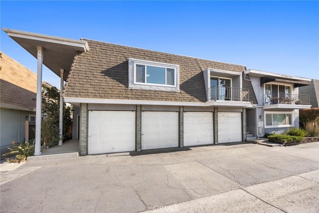 view of front of home featuring driveway, roof with shingles, mansard roof, a balcony, and an attached garage