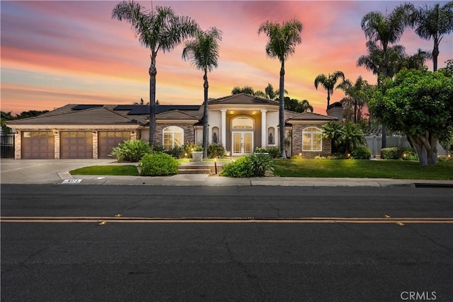 view of front of property with a garage, french doors, a yard, and solar panels