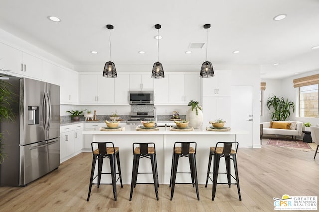 kitchen featuring a kitchen breakfast bar, white cabinetry, appliances with stainless steel finishes, and a center island with sink