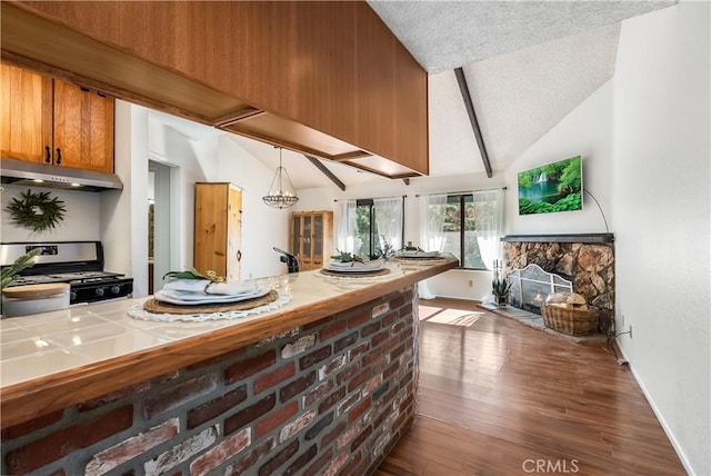 kitchen featuring hardwood / wood-style floors, stainless steel range with gas stovetop, tile counters, a fireplace, and vaulted ceiling with beams